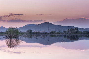 Distant mountain and city, blue hour lake mirror reflection in a calm water of vivid purple sky 