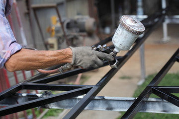 Worker using paint gun to paint metal