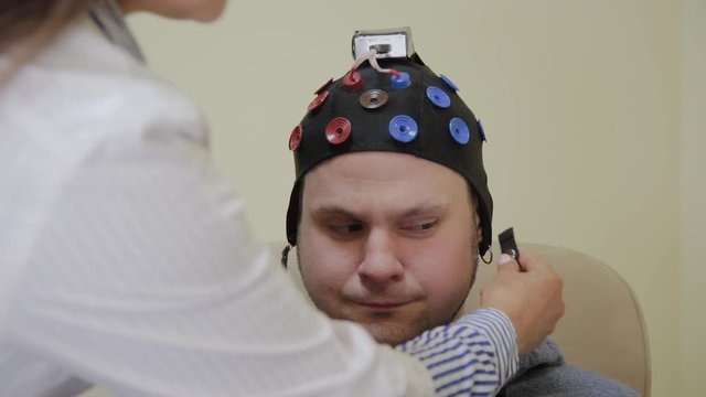 The doctor puts on a man a headset for the study of the human brain.
