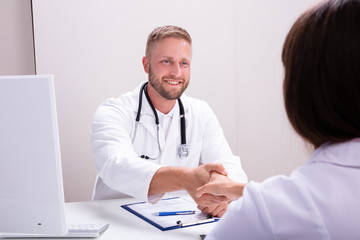 Female And Male Doctor Sitting At Desk Shaking Hands
