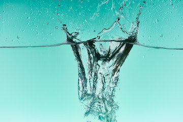 clear ice cubes falling deep in water with splash on turquoise background
