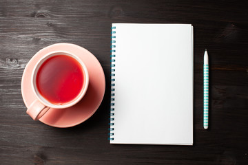 Empty notebook, a cup of tea, pen on black wooden background, top view