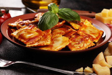 Ravioli with tomato sauce garnished with parmesan cheese and basil on rustic table