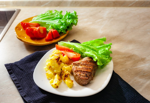 Hot steak on white dish with fried potates and fresh vegetables