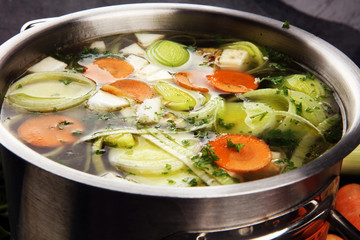 Broth with carrots, onions various fresh vegetables in a pot - colorful fresh clear spring soup. Rural kitchen scenery vegetarian broth