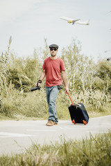 Traveler walking around with a camera in his hand and a backpack. There is a plane in the sky