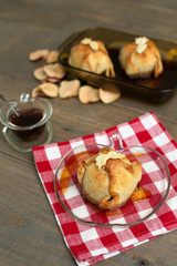 Freshly Baked Homemade Apple Dumplings in Apple Shaped Plate with Red and White Checked Napkin on Wooden Table; Apple Shaped Bowl of Brown Sugar Cinnamon Syrup in Background
