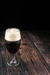 Glass of dark beer with white foam on wooden background. Beverages concept for oktoberfest beer festival with copy space