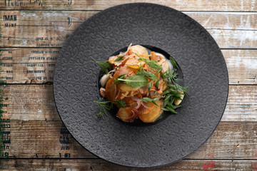 Fried potatoes with garlic and herbs on a black plate on a wooden board