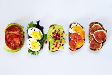 Six different toasts on the white background. Assorted toasts with eggs, fruits and berries, avocado and tomatoes.