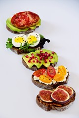 Six different toasts on the white background. Assorted toasts with eggs, fruits and berries, avocado and tomatoes.