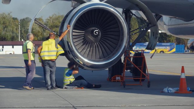 Group of aircraft mechanics and engineers diagnose and repairing jet engine through open hatch. Faces Blurred. Airplane turbine repair.