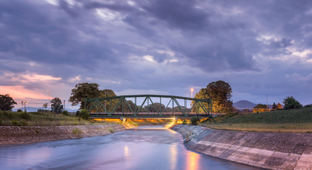 Lighten, iconic, metal railroad bridge in Pirot, Serbia,  over silky water river Nisava and dramatic sunset sky