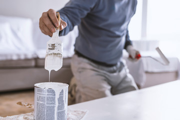 Color brush with paint pot. Hand holding the paint brush and bucket with white color on wood. Loaded Paintbrush after dipping it into bucket. paint running from brush on color can