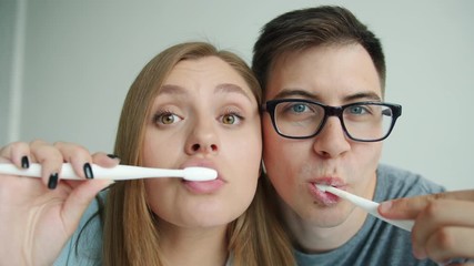 Close-up portrait of happy young people man and woman brushing teeth smiling looking at camera in apartment. Lifestyle, healthcare and youth concept.