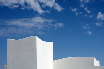 A close sectional view of the top of a white building with a deep blue sky with some white clouds above
