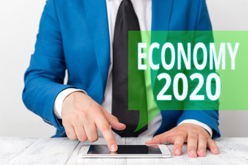 Conceptual hand writing showing Economy 2020. Concept meaning State of wealth and resources of a country in upcoming year Businessman in blue suite with a tie holds lap top in hands