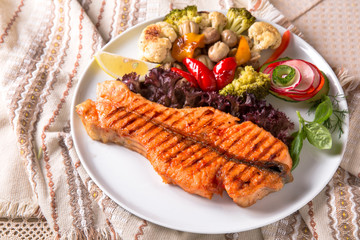 Grilled salmon steak. Juicy delicacy red fish on a plate with a salad of fried vegetables. Balkan cuisine. Restaurant menu