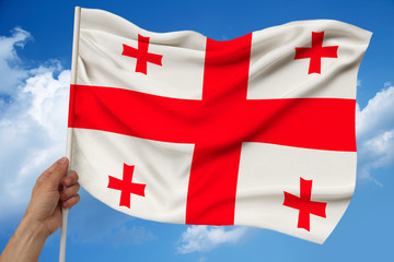 male hand holds against the background of the sky with clouds the national flag of Georgia on a...