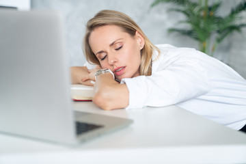 Close up of a tired businesswoman wearing white clothes and sleeping near her laptop in an office...
