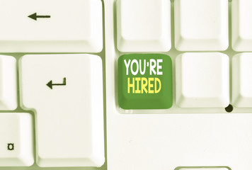 Conceptual hand writing showing You Re Hired. Concept meaning New Job Employed Newbie Enlisted Accepted Recruited White pc keyboard with note paper above the white background