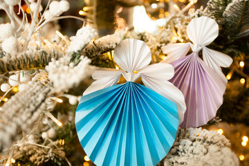 New Year handmade angel papercraft origami figures on christmas tree with holiday decorations with warm lights. Christmas concept winter card studio shot close-up