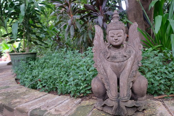 close up one Buddha's wood carving  with wings in front of green plants. In Bagan Myanmar 