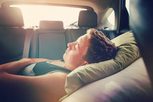 Teenager sleeping in the backseat of a car on a trip
