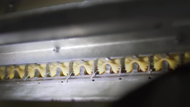 Closeup slow motion of organic pasta butterfly macaroni jumping out of the die of an automated pasta machine in a pasta factory. Food industry.