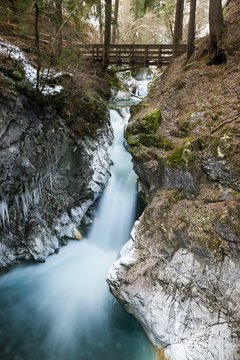 Alpine environment with a waterfall flowing under a wooden bridge surrounded by trees and into a rocky gorge