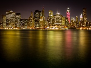 Night shot of Manhattan skyline as seen from Brooklyn Heights, with colorful city lights reflecting on water