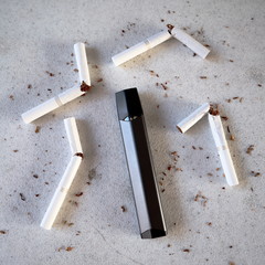 Single vape pen type electronic cigarette as smoking alternative with broken cigarettes and scattered tobacco on white textured background isolated