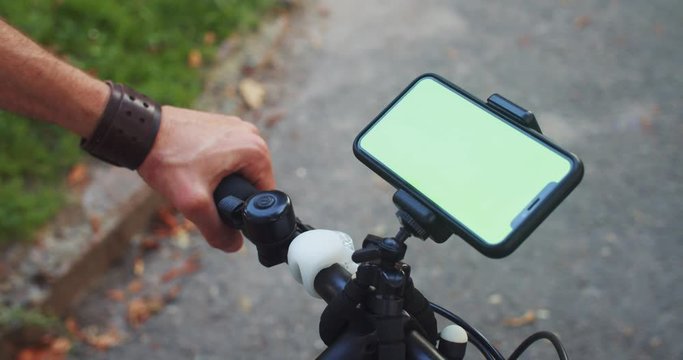 Cyclist using mobile application on smartphone greenscreen mounted on bike handlebar outdoor in the street. Eco transport. Close-up.