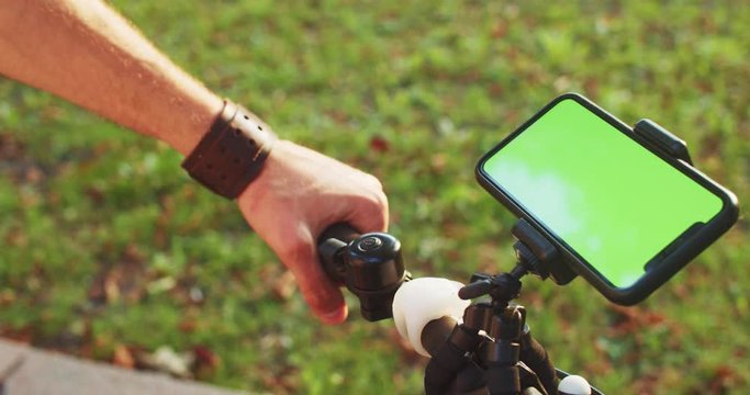 Young man holding modern bike with smartphone mount on handlebars using online map navigator on greenscreen outdoors. Close-up.