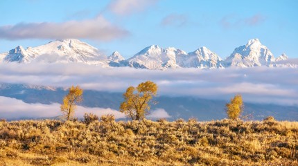 Beautiful autumn landscape scene with snowcapped Grand Teton mountain range and low lying clouds. Jackson Hole, Wyoming.