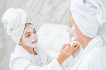 Young girl puts white cream on her mother's face at home
