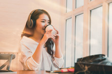 Young woman drinking coffee and enjoy listening to music with headphones relaxing at home. Warm tone.