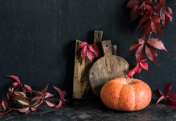Fall still life. Rustic cutting boards, leaf branches, pumpkin on the table, on a dark background....