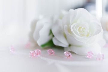 Close up of a white rose lying on a table among pink crystals against a bokeh background