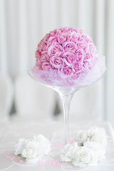Close up of a wedding decoration consisting in a huge chalice filled with a bouquet of pink roses against a white bokeh background