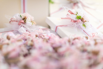 In the foreground there are a number of out of focus party favors; in the background there is white gift box with pink and white ribbon