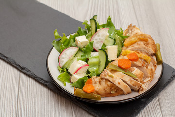 Plate with meat, vegetable salad with cheese, cucumber and radish on stone board.