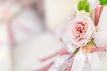 Close up of a decorazione made up of a pink rose and a white and pink ribbon against a bright bokeh background