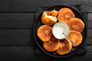 Cottage cheese pancakes on a black background. Syrniki with sour cream and jam.