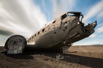 Wide angle shot of an old and abandoned DC-3 plane in the icelandic desert, with trailing couds in the background