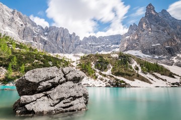 Long exposure of the Sorapis lake in northern Italy, with its light blue water and a boulder in the foreground