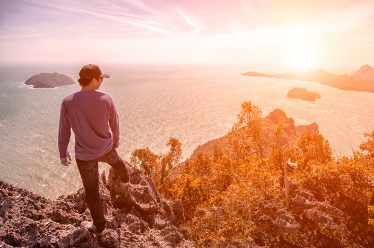 Men in blue shirts are looking at the beauty of the sea on the hilltop with sunset over the sea. Men are looking at the success of climbing.