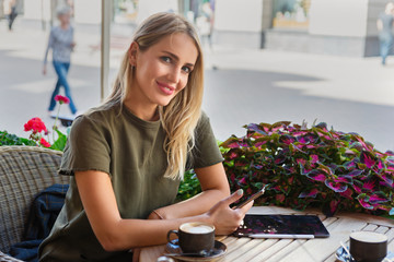 A woman with smiley face holding and using Ipad tablet pc while drinking coffee in modern cafe