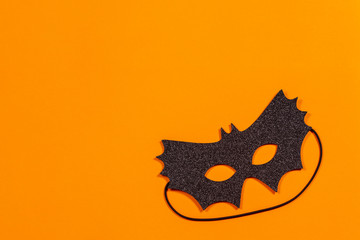 Black halloween mask on orange background, top view