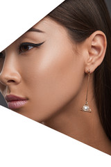 Closeup side view shot of woman with straight dark hair wearing golden metallic earring with a pearl bead. The girl with bronze skin has bright make-up: long dark wings and pink pearly lipstick. 